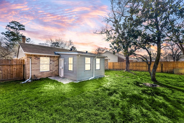 back house at dusk featuring a lawn