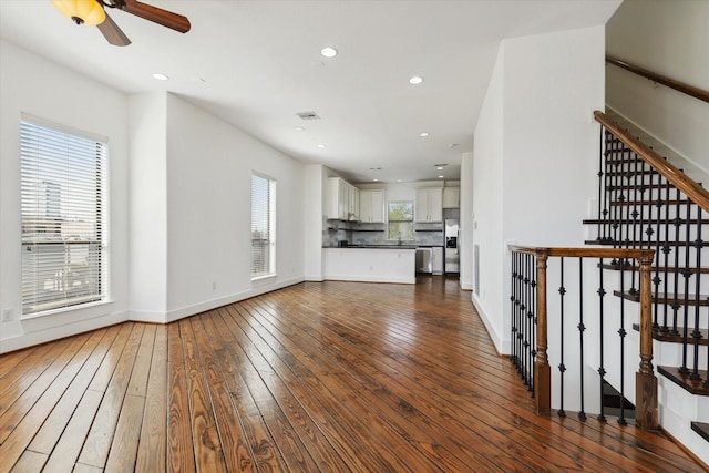 unfurnished living room with hardwood / wood-style floors, stairway, visible vents, and baseboards