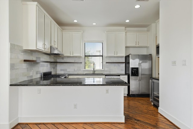 kitchen with stainless steel fridge, tasteful backsplash, dark wood-style floors, a peninsula, and a sink