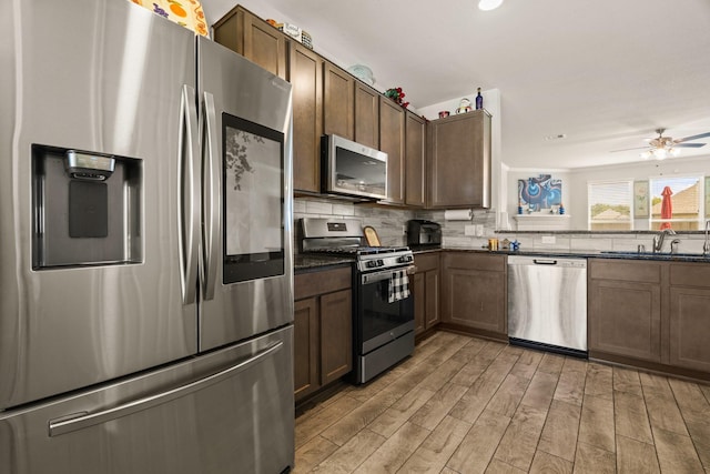 kitchen featuring appliances with stainless steel finishes, sink, backsplash, ceiling fan, and light hardwood / wood-style flooring