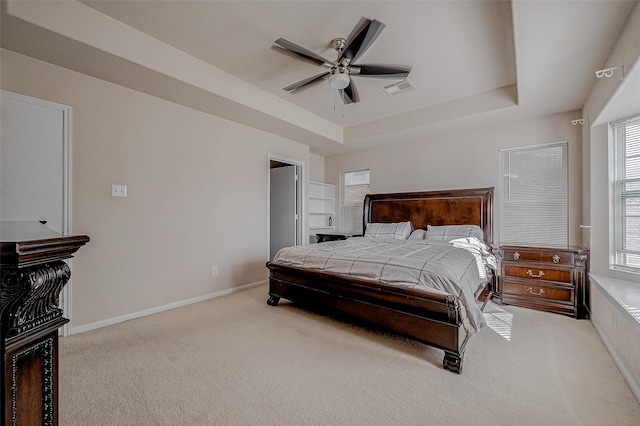 bedroom with light colored carpet, ceiling fan, and a tray ceiling