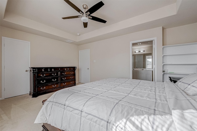 bedroom featuring a raised ceiling, connected bathroom, light colored carpet, and ceiling fan