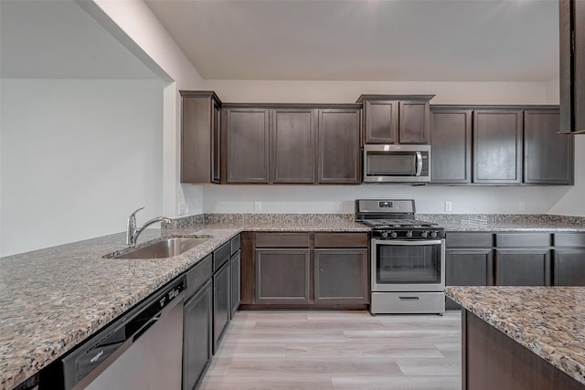 kitchen with sink, stainless steel appliances, light stone countertops, dark brown cabinets, and light hardwood / wood-style flooring