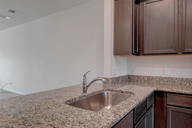 kitchen with light stone counters, sink, and dark brown cabinets