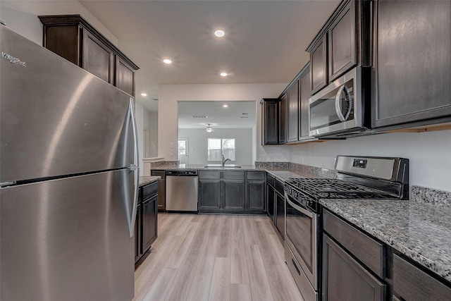 kitchen with dark brown cabinetry, sink, light stone counters, stainless steel appliances, and light hardwood / wood-style floors