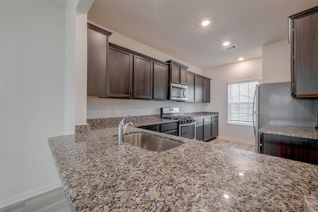 kitchen with stainless steel appliances, dark brown cabinets, sink, and light stone counters