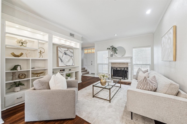 living room with dark wood-type flooring, a fireplace, crown molding, and built in features