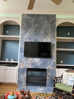 unfurnished living room featuring ceiling fan, wood-type flooring, ornamental molding, and a fireplace