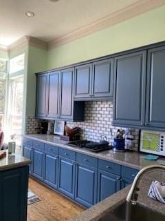 kitchen with stainless steel gas stovetop, tasteful backsplash, ornamental molding, blue cabinetry, and light hardwood / wood-style flooring