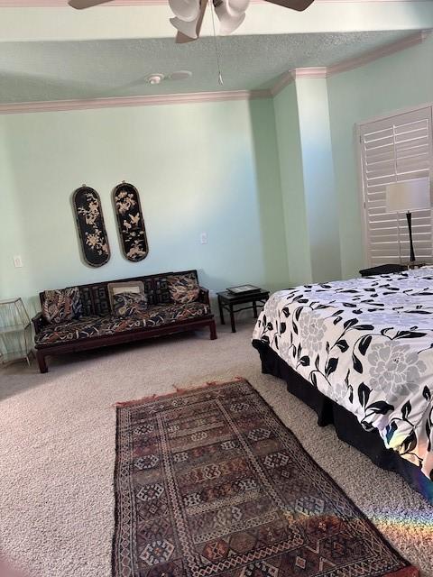 carpeted bedroom with ceiling fan, ornamental molding, and a textured ceiling