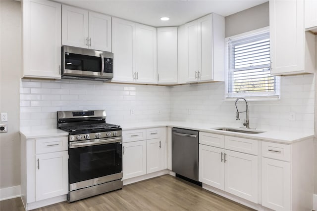 kitchen featuring sink, tasteful backsplash, light wood-type flooring, appliances with stainless steel finishes, and white cabinets