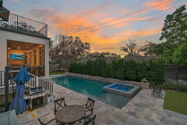 pool at dusk with a grill, a patio area, and an in ground hot tub