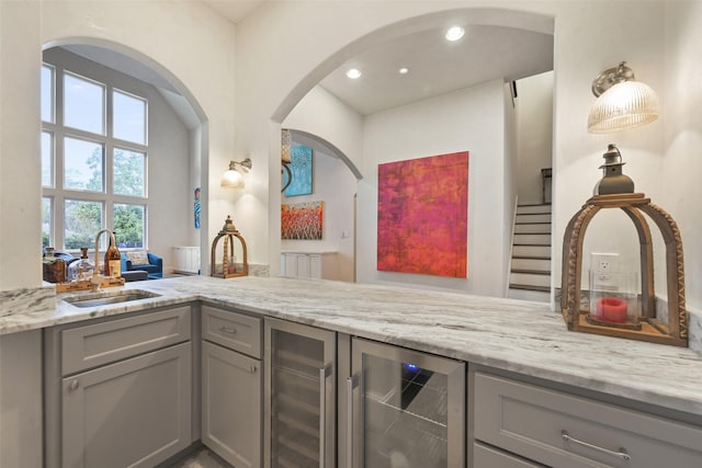 kitchen featuring light stone counters, beverage cooler, sink, and gray cabinetry