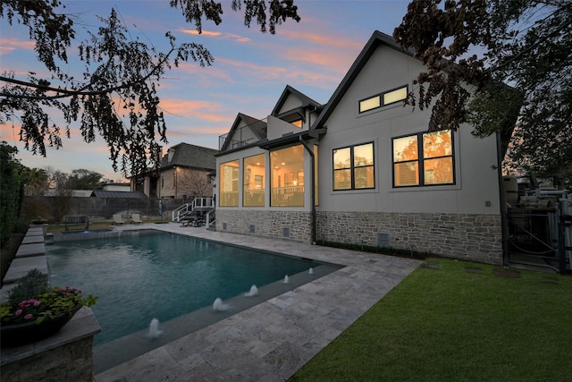 back house at dusk with a balcony, a yard, a fenced in pool, and a patio area