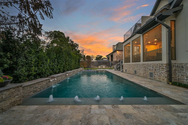 pool at dusk featuring pool water feature