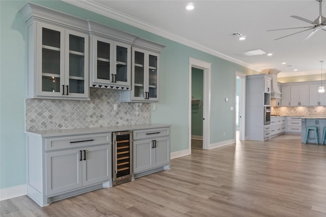 bar featuring light wood-style flooring, ornamental molding, beverage cooler, and oven