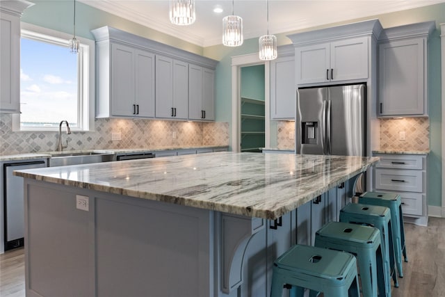 kitchen with a large island, ornamental molding, light stone counters, appliances with stainless steel finishes, and light wood finished floors