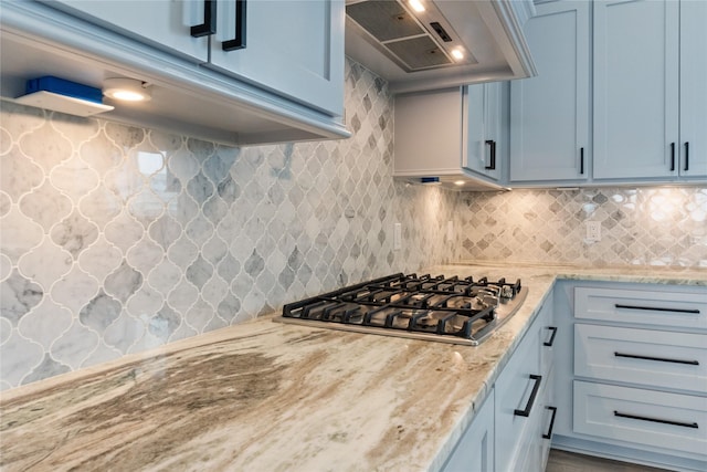 kitchen featuring light stone counters, decorative backsplash, stainless steel gas cooktop, and wall chimney exhaust hood