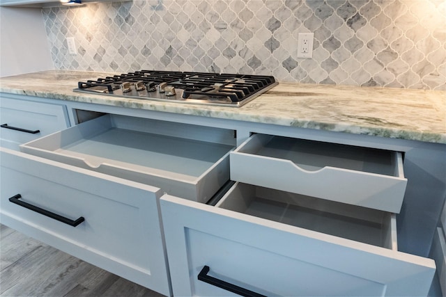 interior details with decorative backsplash, light stone countertops, stainless steel gas stovetop, and wood finished floors