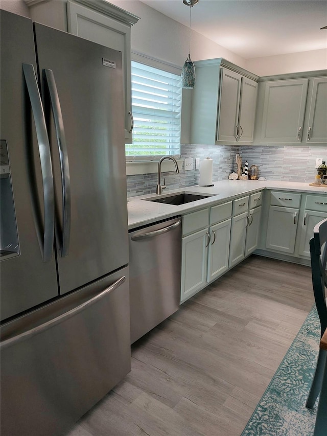 kitchen with appliances with stainless steel finishes, sink, backsplash, and light wood-type flooring