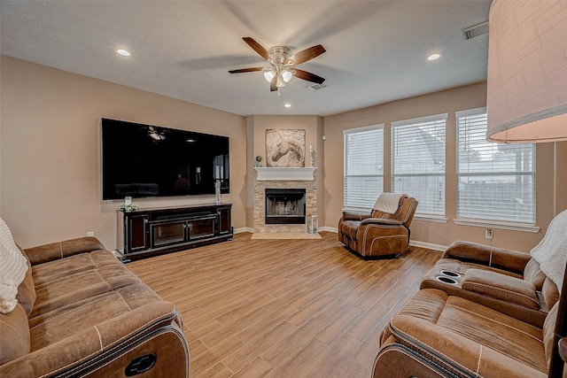 living room featuring ceiling fan, a fireplace, and light wood-type flooring