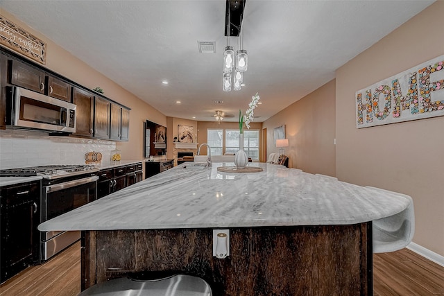 kitchen featuring stainless steel appliances, dark brown cabinetry, a large island with sink, and decorative light fixtures