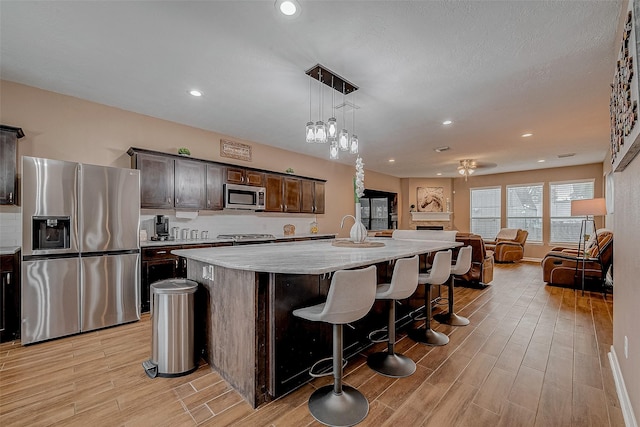 kitchen featuring dark brown cabinets, stainless steel appliances, a center island with sink, a kitchen bar, and decorative light fixtures