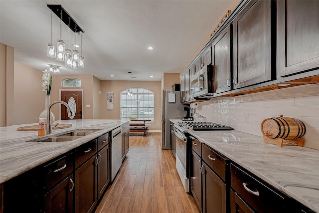 kitchen with hanging light fixtures, appliances with stainless steel finishes, sink, and light stone counters