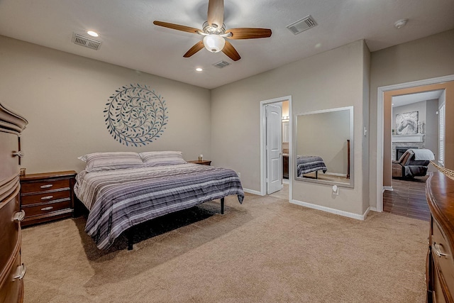 bedroom featuring a stone fireplace, light colored carpet, and ceiling fan