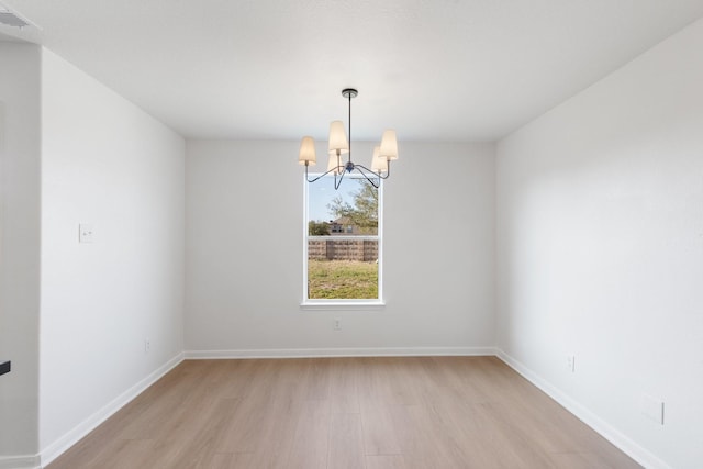 spare room with a notable chandelier and light wood-type flooring