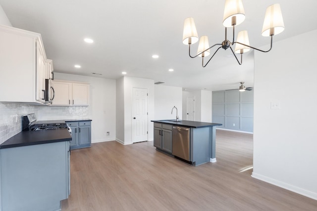 kitchen featuring sink, appliances with stainless steel finishes, white cabinetry, a center island with sink, and decorative light fixtures