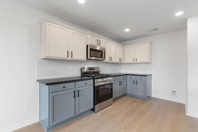 kitchen with appliances with stainless steel finishes, white cabinetry, gray cabinetry, decorative backsplash, and light wood-type flooring