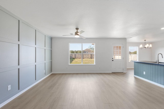 unfurnished living room featuring ceiling fan with notable chandelier, sink, a textured ceiling, and light wood-type flooring