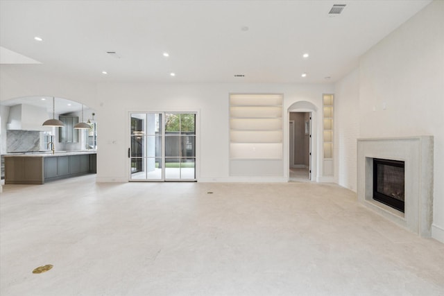 unfurnished living room with arched walkways, built in shelves, visible vents, and recessed lighting