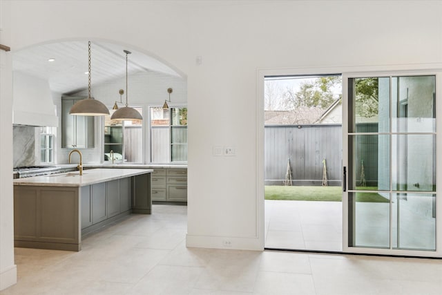 kitchen featuring decorative backsplash, gray cabinetry, a healthy amount of sunlight, premium range hood, and pendant lighting