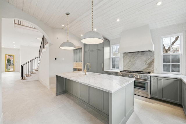 kitchen with a kitchen island with sink, gray cabinetry, premium range hood, a sink, and high end range