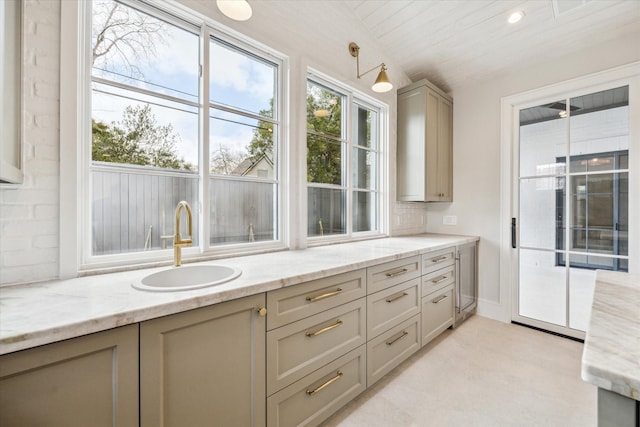 kitchen featuring light stone countertops, a sink, vaulted ceiling, decorative backsplash, and decorative light fixtures