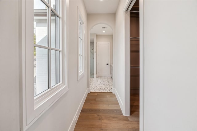 hallway with light wood-style floors, arched walkways, and baseboards