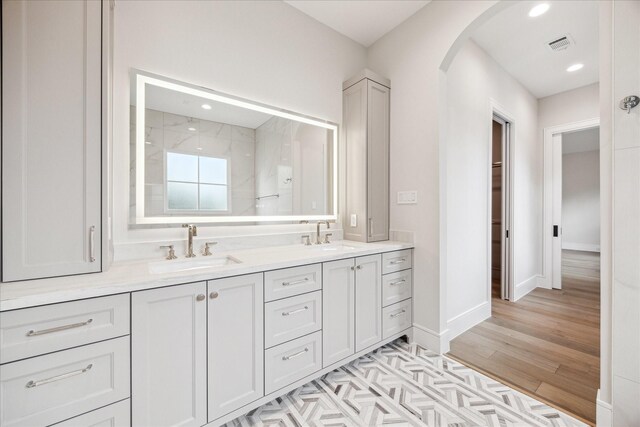 full bath featuring double vanity, wood finished floors, a sink, and visible vents