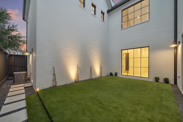 rear view of property featuring central AC unit, fence, a lawn, and brick siding