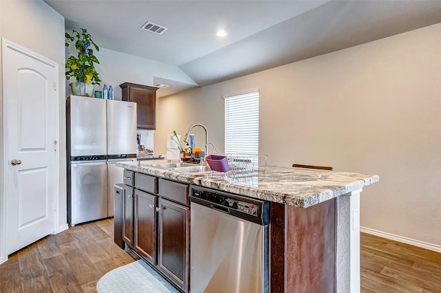 kitchen with dark brown cabinetry, sink, hardwood / wood-style flooring, stainless steel appliances, and a kitchen island with sink