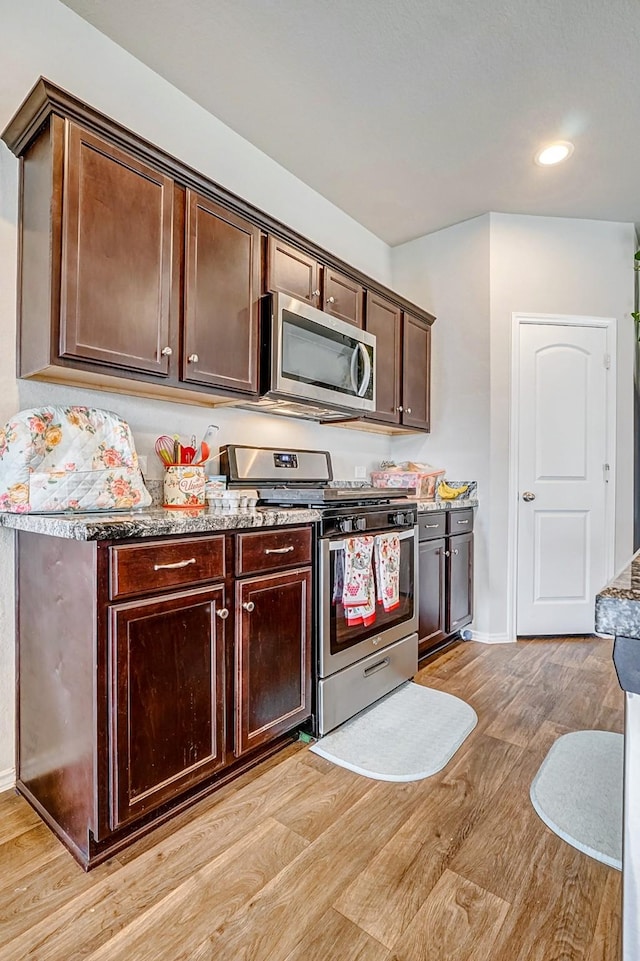 kitchen with light stone counters, dark brown cabinets, stainless steel appliances, and light wood-type flooring