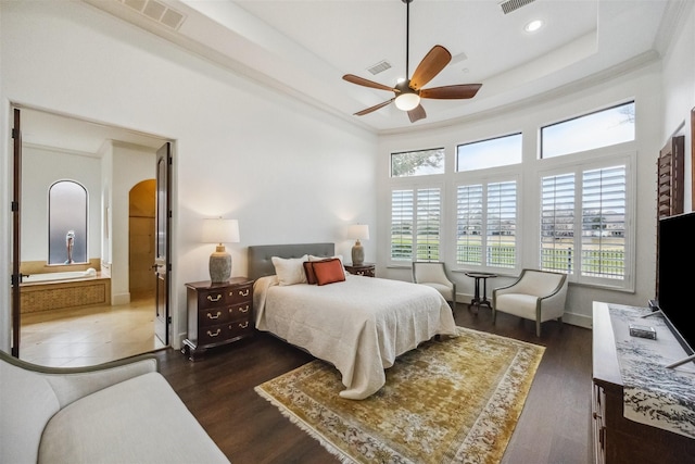 bedroom featuring dark wood-type flooring, ceiling fan, connected bathroom, a tray ceiling, and ornamental molding