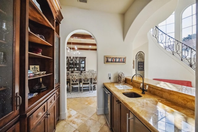 bar with sink, beam ceiling, stainless steel dishwasher, and light stone countertops