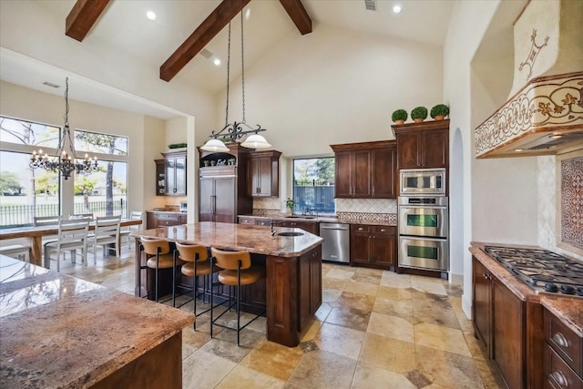 kitchen featuring a breakfast bar, decorative light fixtures, a kitchen island with sink, built in appliances, and light stone countertops