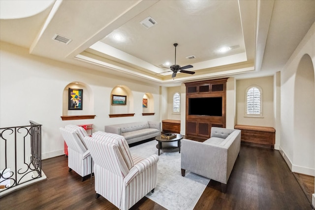 living room with dark wood-type flooring, a raised ceiling, and ceiling fan