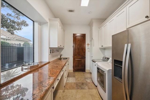 kitchen with light stone counters, stainless steel fridge with ice dispenser, washer and clothes dryer, and white cabinets