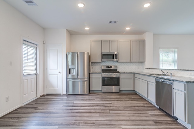 kitchen with appliances with stainless steel finishes, tasteful backsplash, sink, light stone countertops, and light hardwood / wood-style flooring