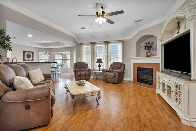 living room featuring crown molding, a raised ceiling, ceiling fan, a fireplace, and light hardwood / wood-style floors