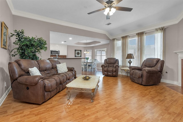 living room with a raised ceiling, ornamental molding, ceiling fan, and light wood-type flooring